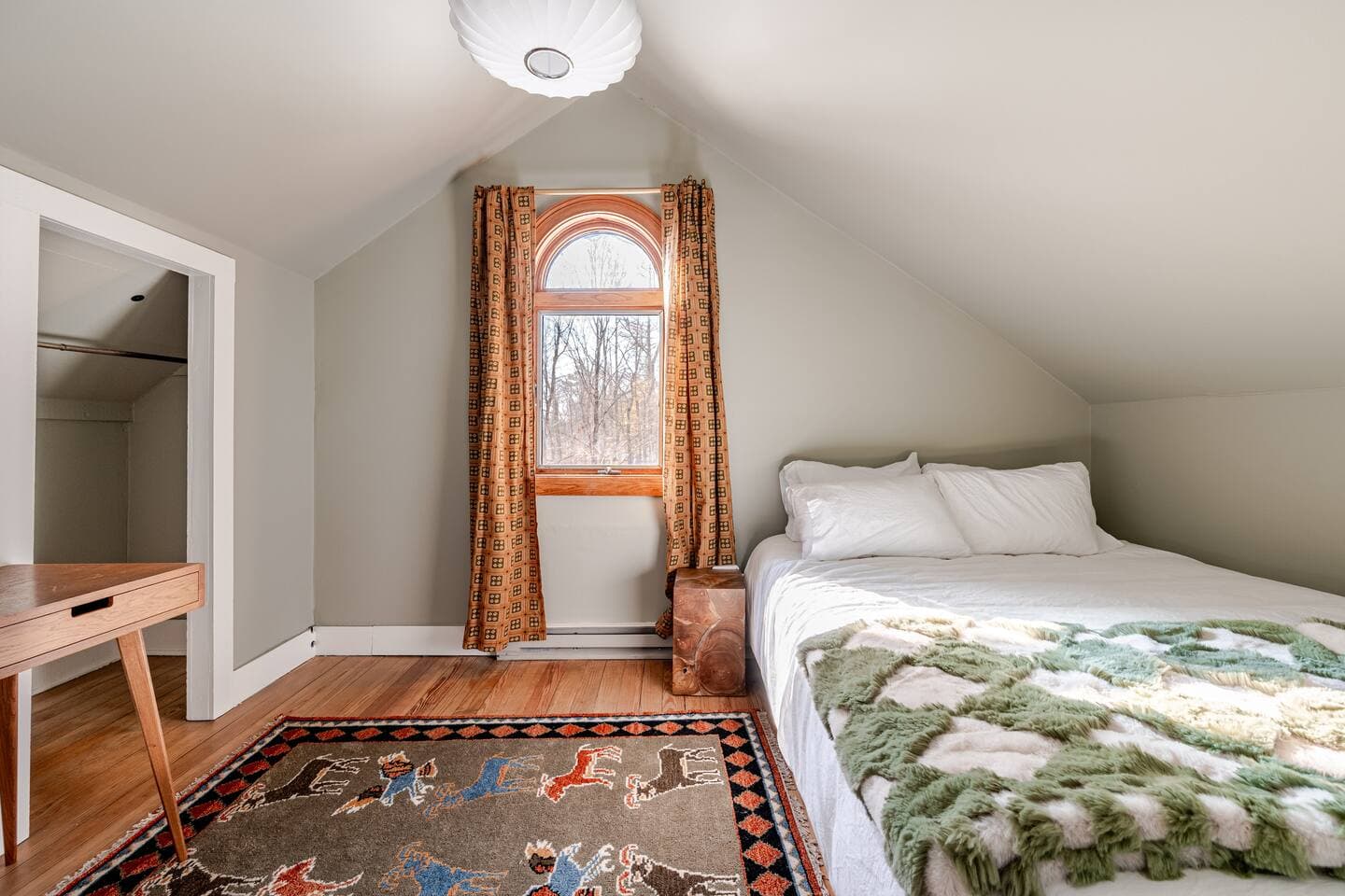 Loft bedroom with queen bed, arched window, and writing desk at The Cedar Stock Cabin